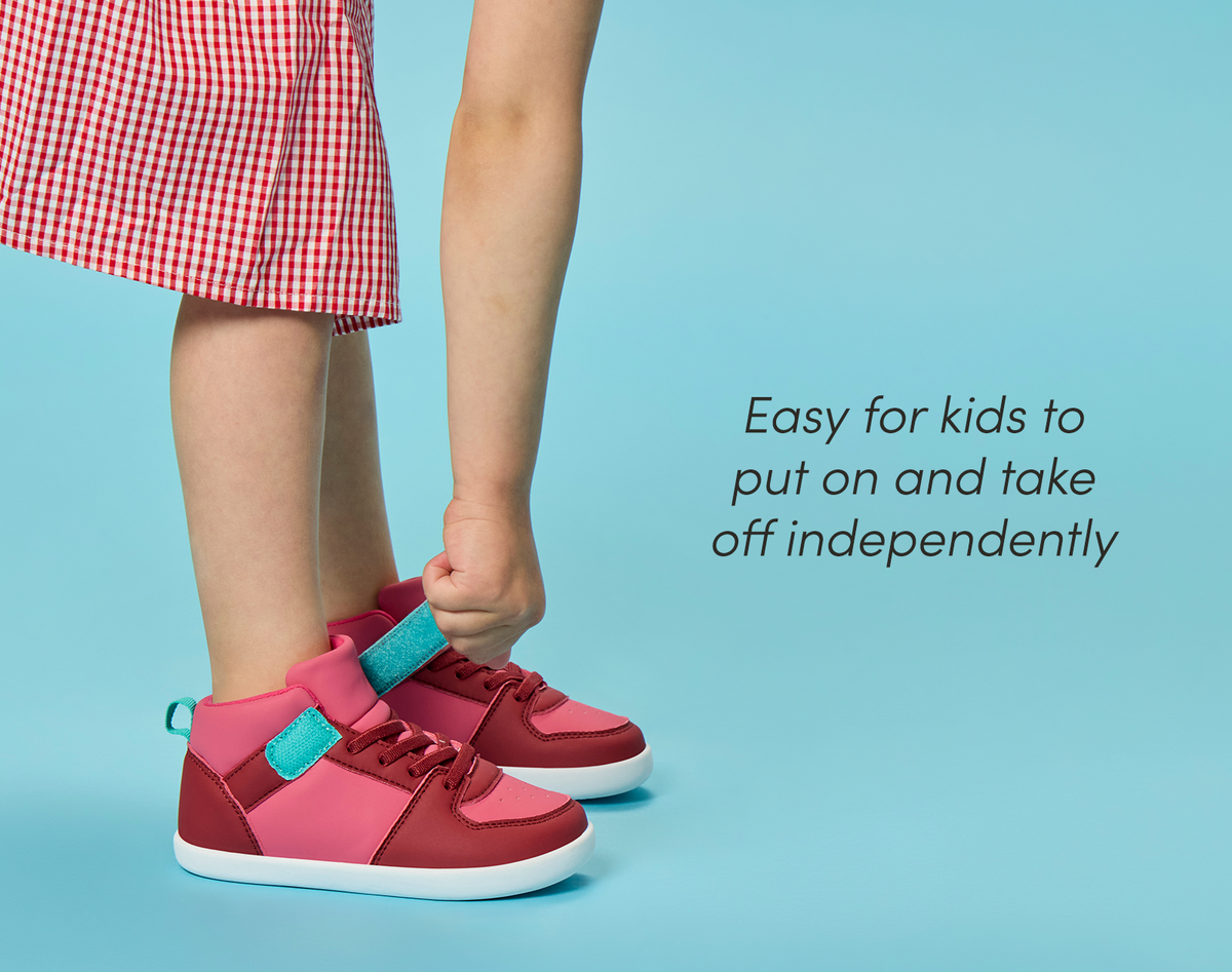 Side view child adjusting strap of Ten Little Varsity Mid Tops, easy for kids to put on and take off independently - All Star Pink. Available at www.tenlittle.com